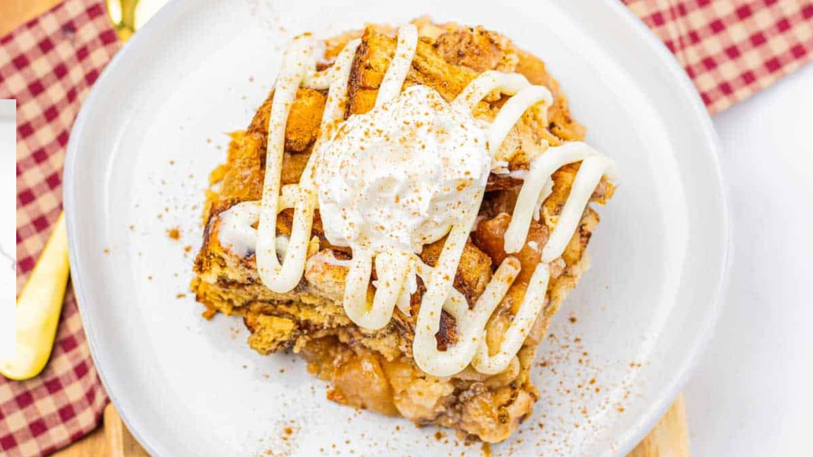 A slice of apple dessert topped with whipped cream and icing drizzle on a white plate.