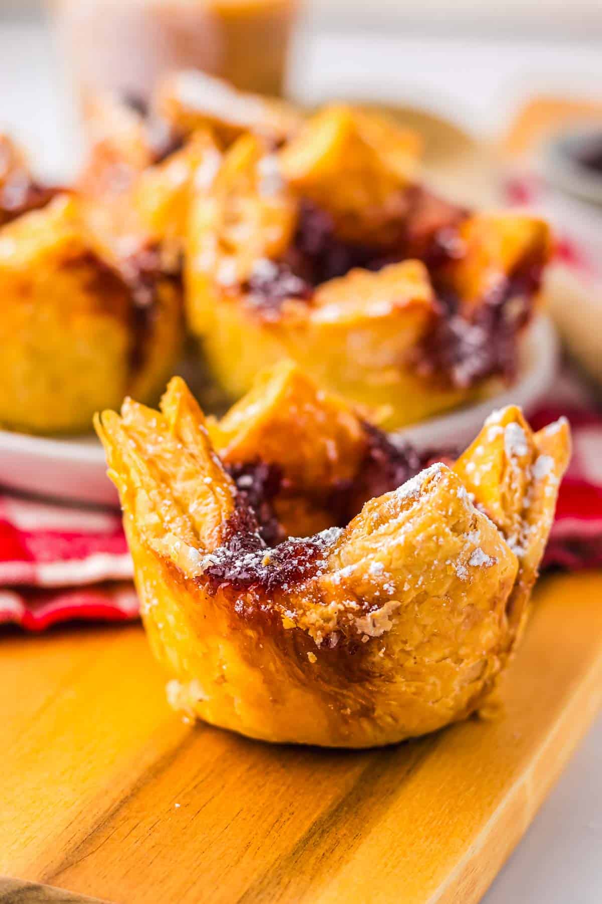 Golden, flaky pastry cups reminiscent of a Starbucks Copycat Sugar Plum Cheese Danish, filled with jam and dusted with powdered sugar, displayed on a wooden board.