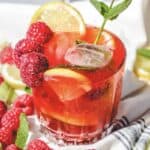 A glass of red drink with fruit and mint, perfect for enjoying a refreshing raspberry mojito mocktail recipe.