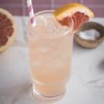 A refreshing pink grapefruit mocktail recipe with ice, a striped straw, and a grapefruit wedge garnish on a marble surface&mdash;perfect for sipping and boosting your electrolyte levels.