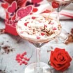 A martini glass filled with whipped dessert, heart sprinkles, and a red rose nearby&mdash;perfect for a Valentine celebration or as a decadent Red Velvet treat.