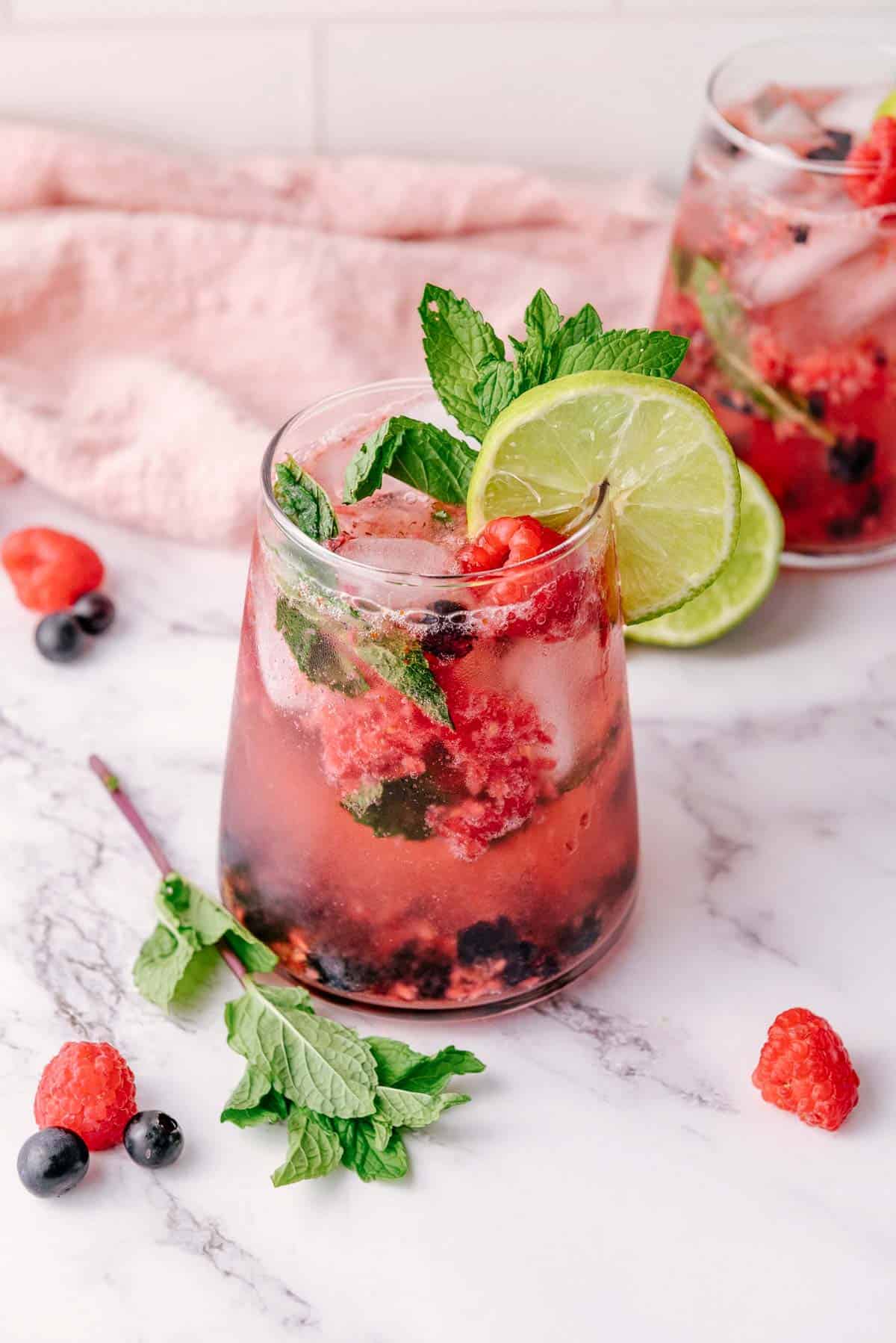 A refreshing mint mocktail, this berry mojito is garnished with lime, fresh mint, and raspberries, served in a glass on a marble surface.