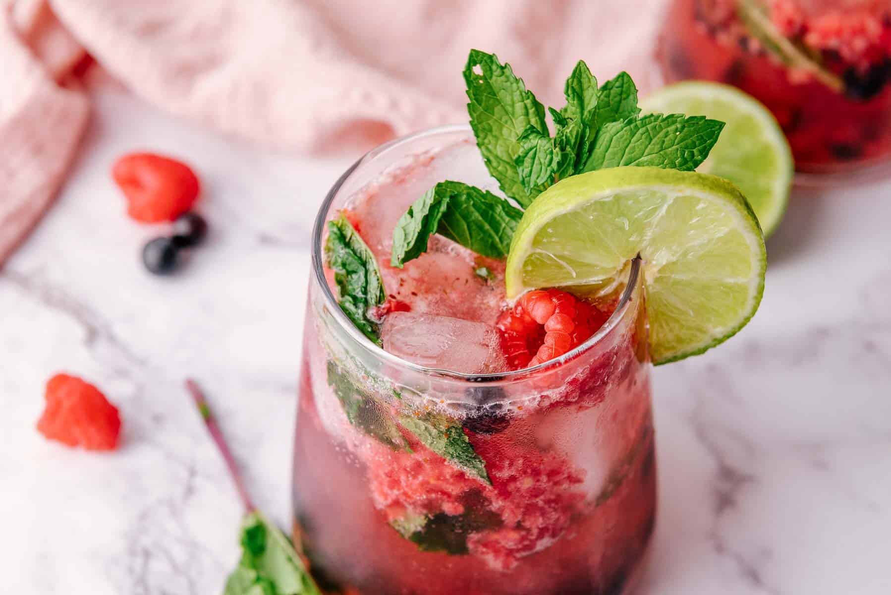 A refreshing blueberry raspberry mocktail garnished with lime slices, fresh mint, and raspberries on a marble surface.