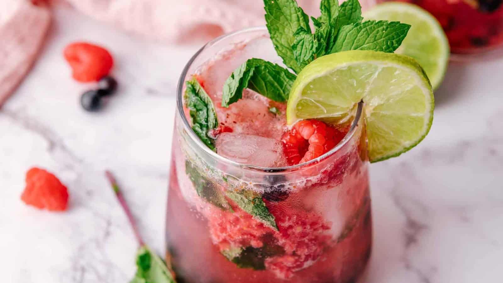 A refreshing berry cocktail with lime slices, mint leaves, and ice on a marble surface.