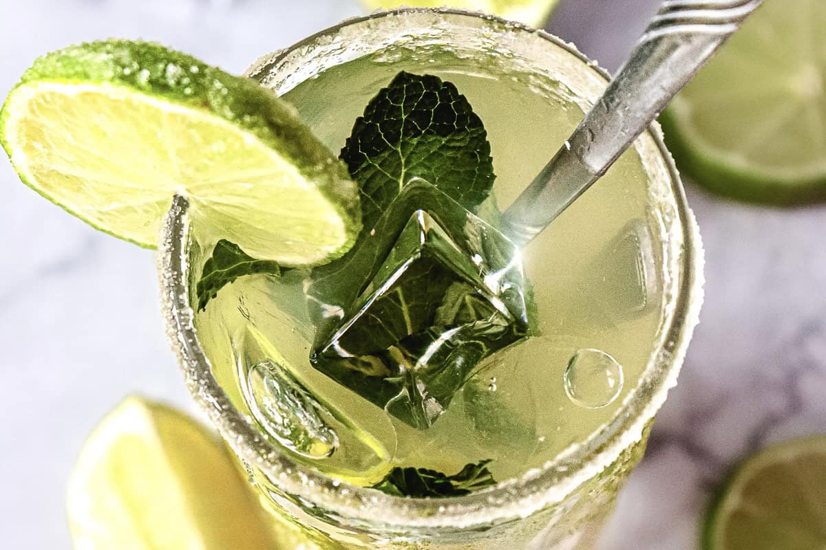A refreshing Virgin Mojito mocktail served in a glass with lime slices, mint leaves, ice cubes, and a straw on a light background.