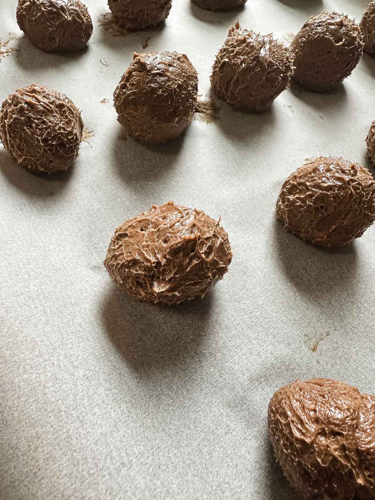 Chocolate truffles with a rough texture, made from an easy truffle recipe, are arranged on a sheet of parchment paper.