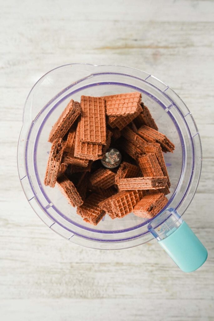 Chocolate wafer cookies in a food processor, ready to be blended for easy dessert recipes like chocolate truffles, on a light wooden surface.
