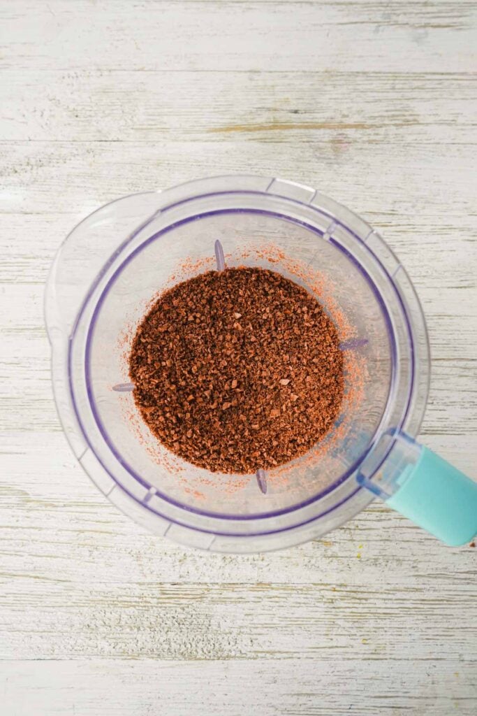 Ground chocolate mixture for easy truffle recipe in a blender, viewed from above on a white wooden surface.