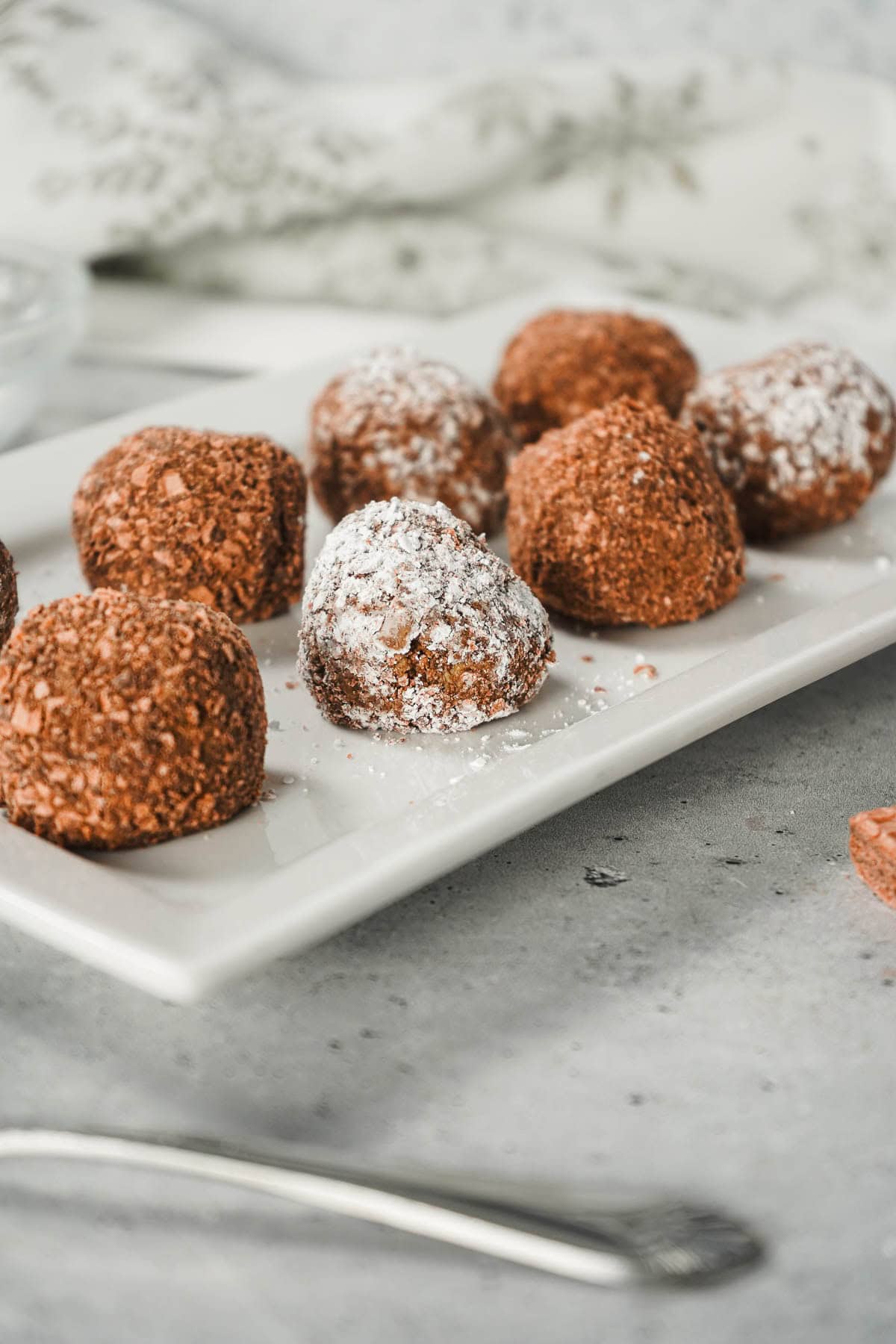 Chocolate Mint Truffles dusted with powdered sugar on a white rectangular plate, with a fork nearby&mdash;an easy truffle recipe for any occasion.