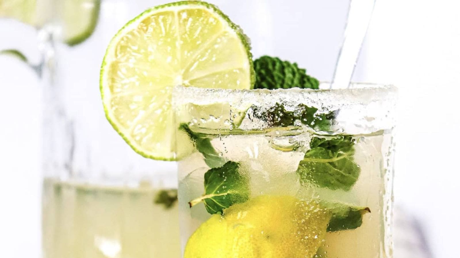 A glass of mojito with lime, mint, lemon, ice, and a sugared rim.