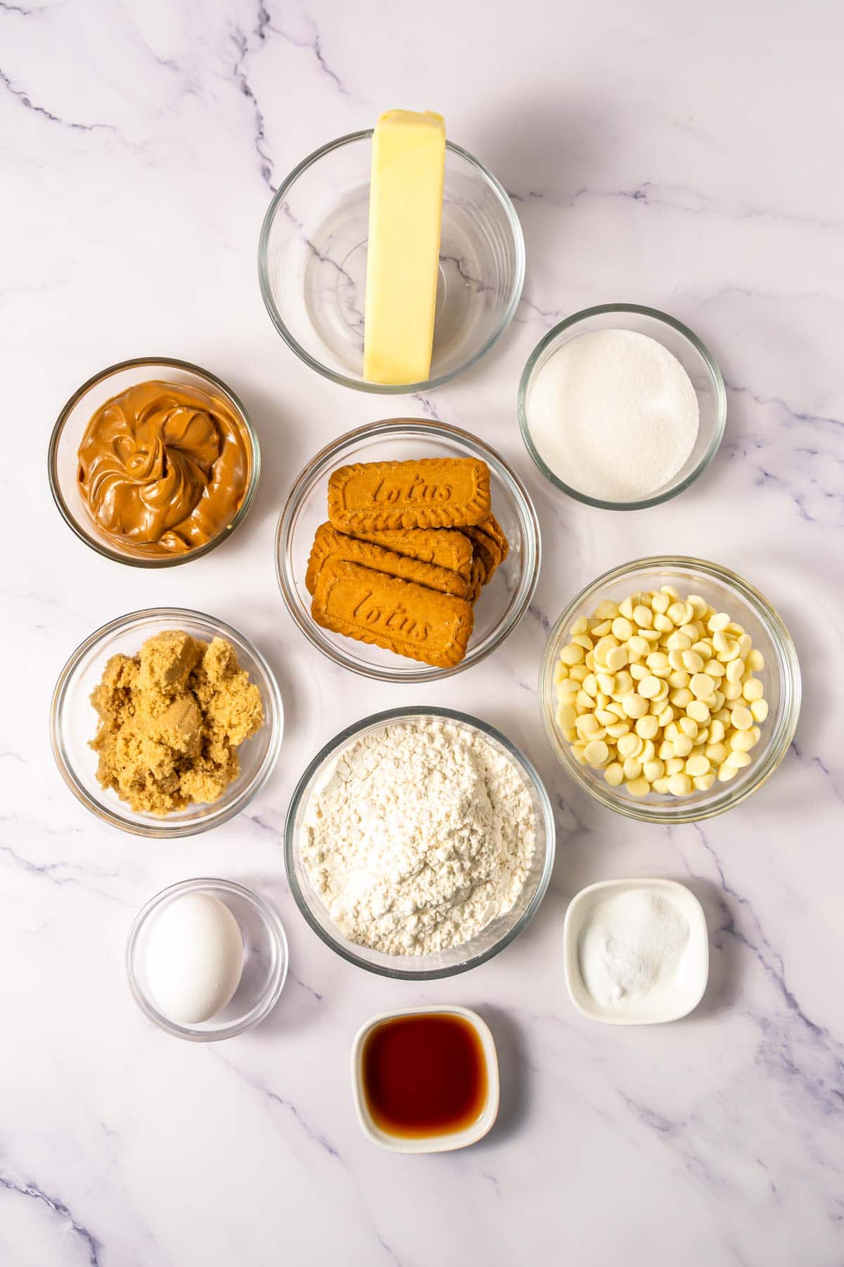 Bowls of ingredients for baking Crumbl Biscoff cookies: butter, sugars, flour, egg, Biscoff cookies, spread, white chocolate chips, and vanilla.