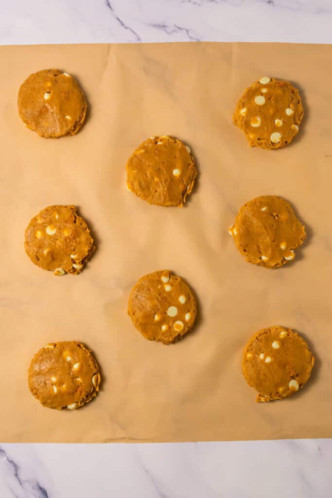 Eight unbaked Copycat Crumbl cookie dough balls with white chocolate chips are arranged in rows on parchment paper.