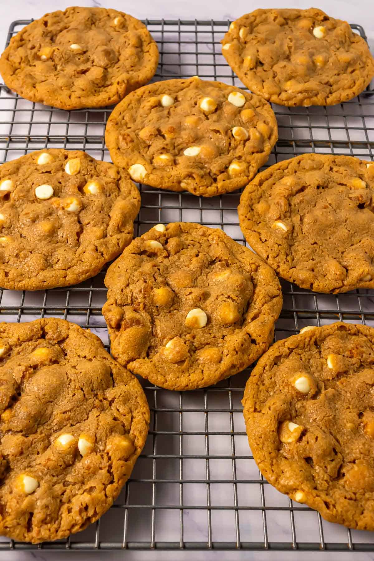 Eight Crumbl Copycat white chocolate chip cookies cooling on a wire rack.