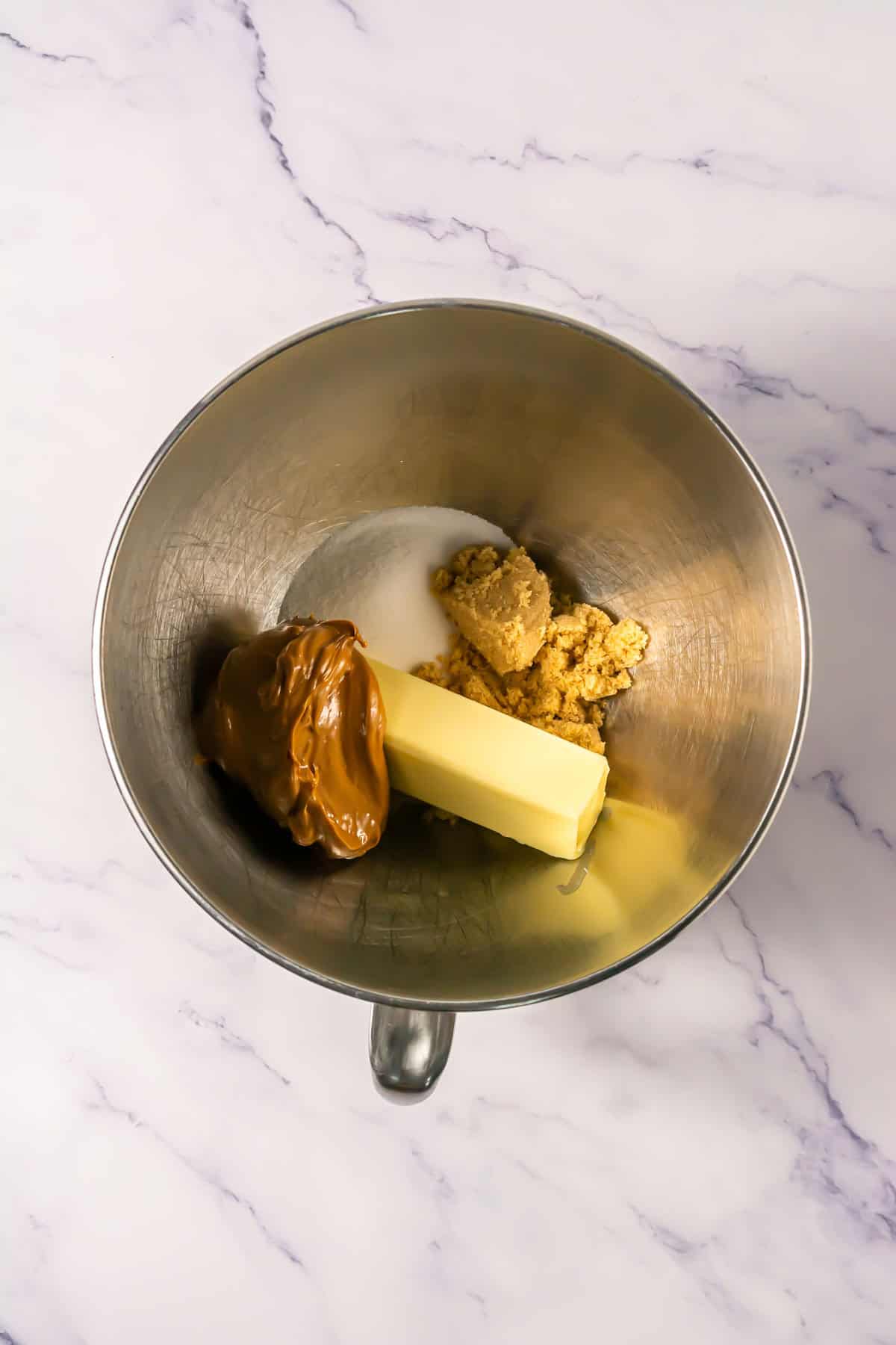 A mixing bowl with butter, brown sugar, white sugar, and a large dollop of peanut butter inside&mdash;perfect for starting your next Crumbl copycat or Biscoff cookies copycat recipe.
