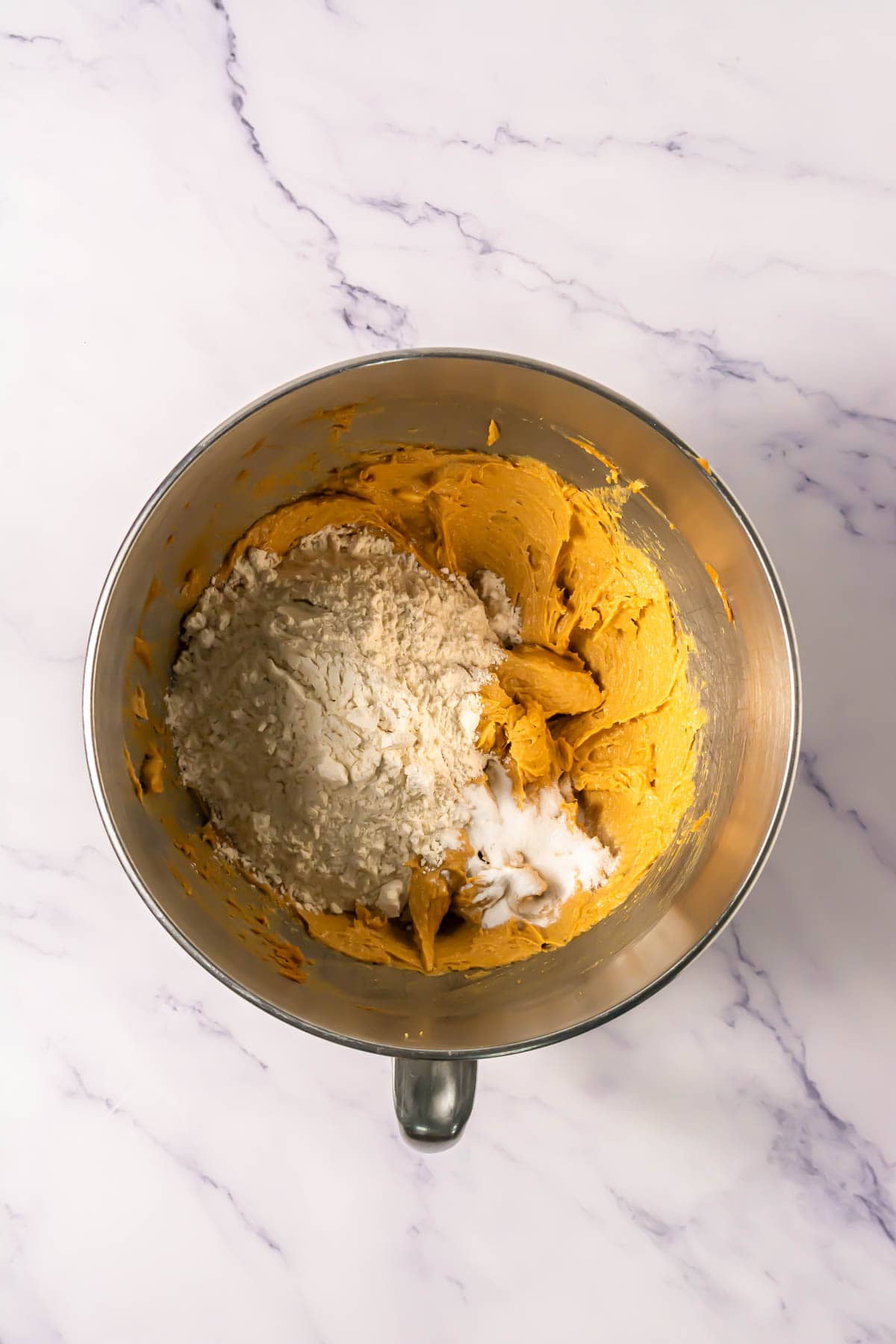 Mixing bowl with cookie dough, oats, and coconut on a marble surface, viewed from above&mdash;perfect for making Crumbl Copycat cookies.