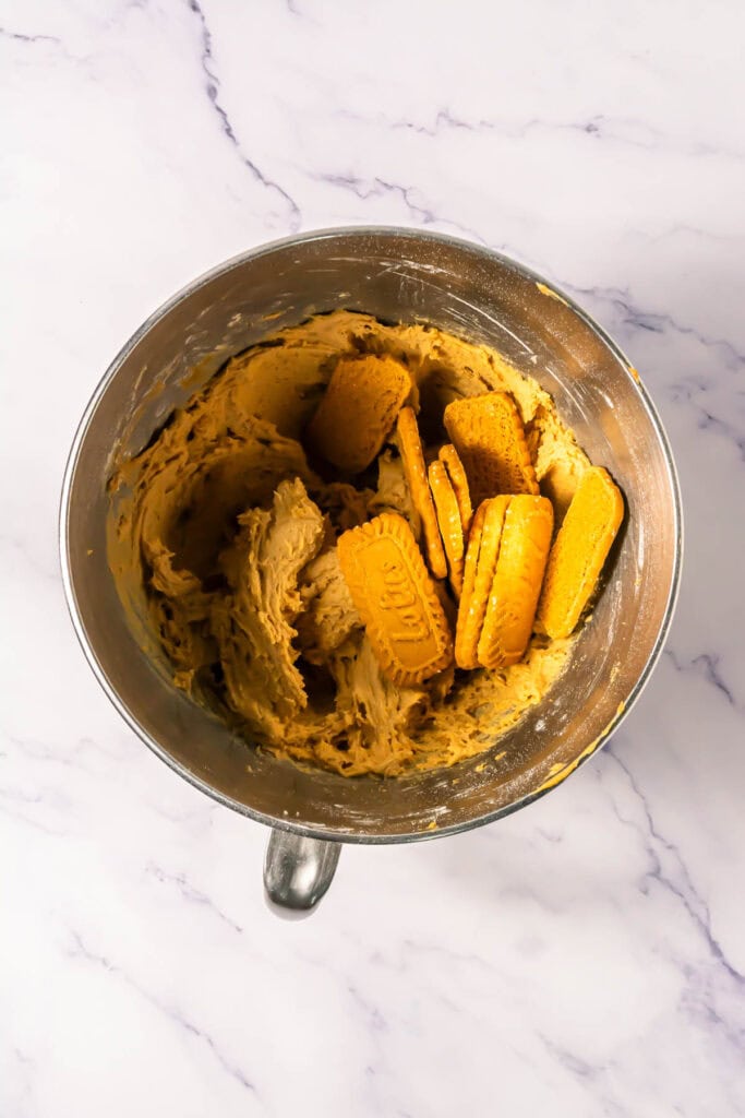 Mixing bowl with creamy dough and several rectangular golden Biscoff cookies on top, perfect for a Crumbl copycat recipe, on a marble surface.