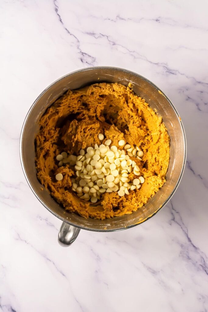 A metal mixing bowl with cookie dough and white chocolate chips on a marble countertop, perfect for making your favorite Crumbl copycat or Biscoff cookies.
