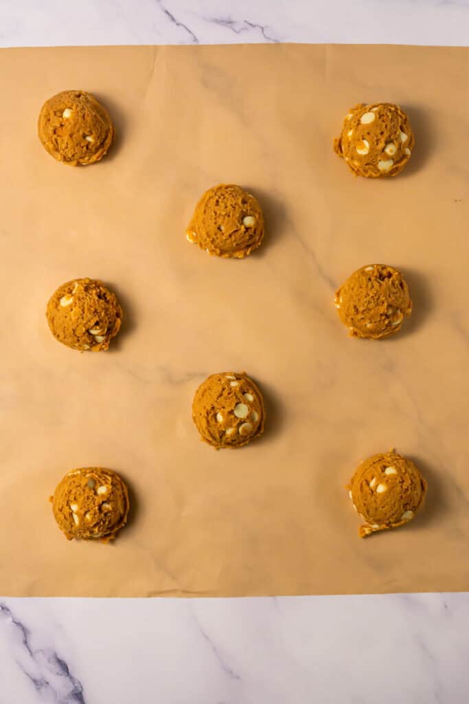 Eight scoops of Crumbl Copycat cookie dough with white chocolate chips on parchment paper, ready to bake.