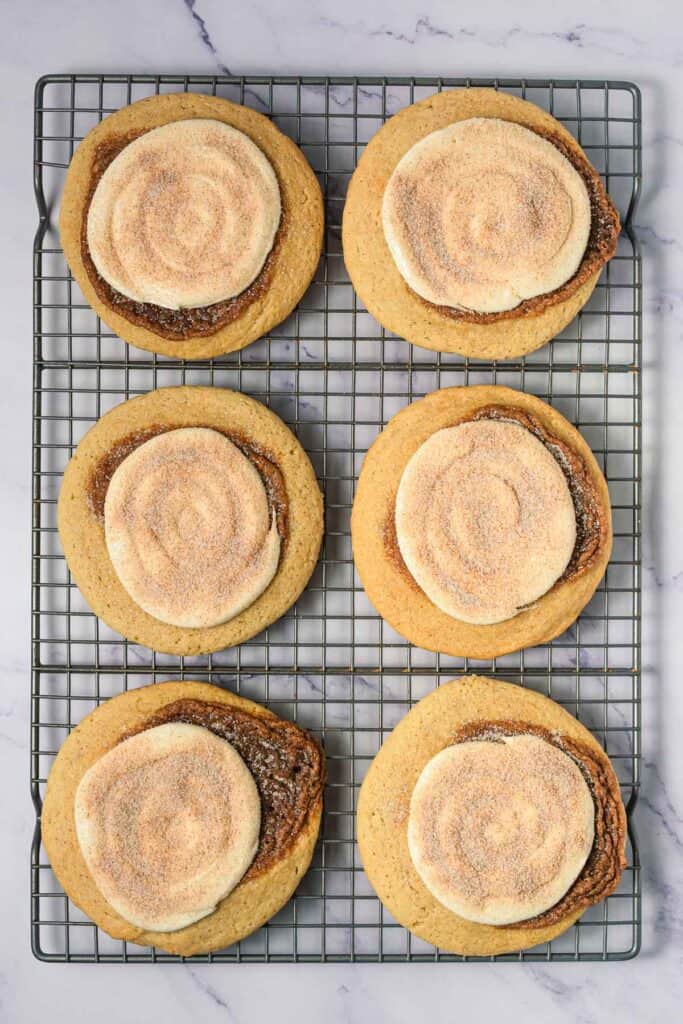 Six large cinnamon swirl cookies with sugary topping, just like Crumbl copycat treats, cooling on a rack atop a marble surface.