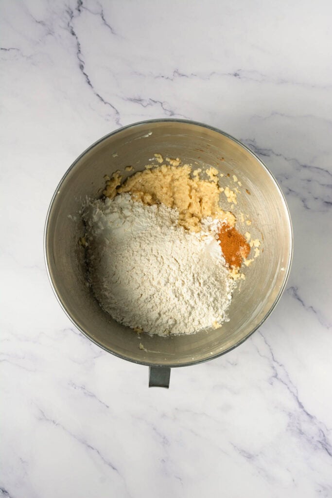A mixing bowl with sugar, flour, and spices on a marble countertop, ready to be combined for delicious Crumbl copycat or cinnamon swirl cookies.
