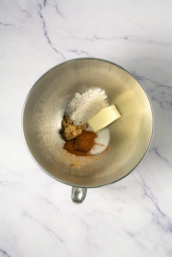 A mixing bowl with butter, flour, brown sugar, white sugar, and cinnamon on a marble surface&mdash;perfect for making delicious Copycat Cookies or Cinnamon Swirl Cookies.