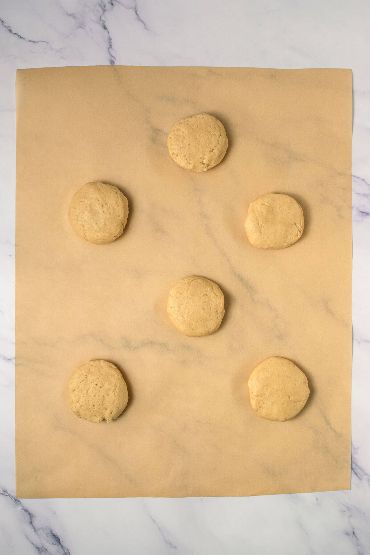 Six unbaked Crumbl copycat cookies arranged on parchment paper on a marble surface, ready for baking.