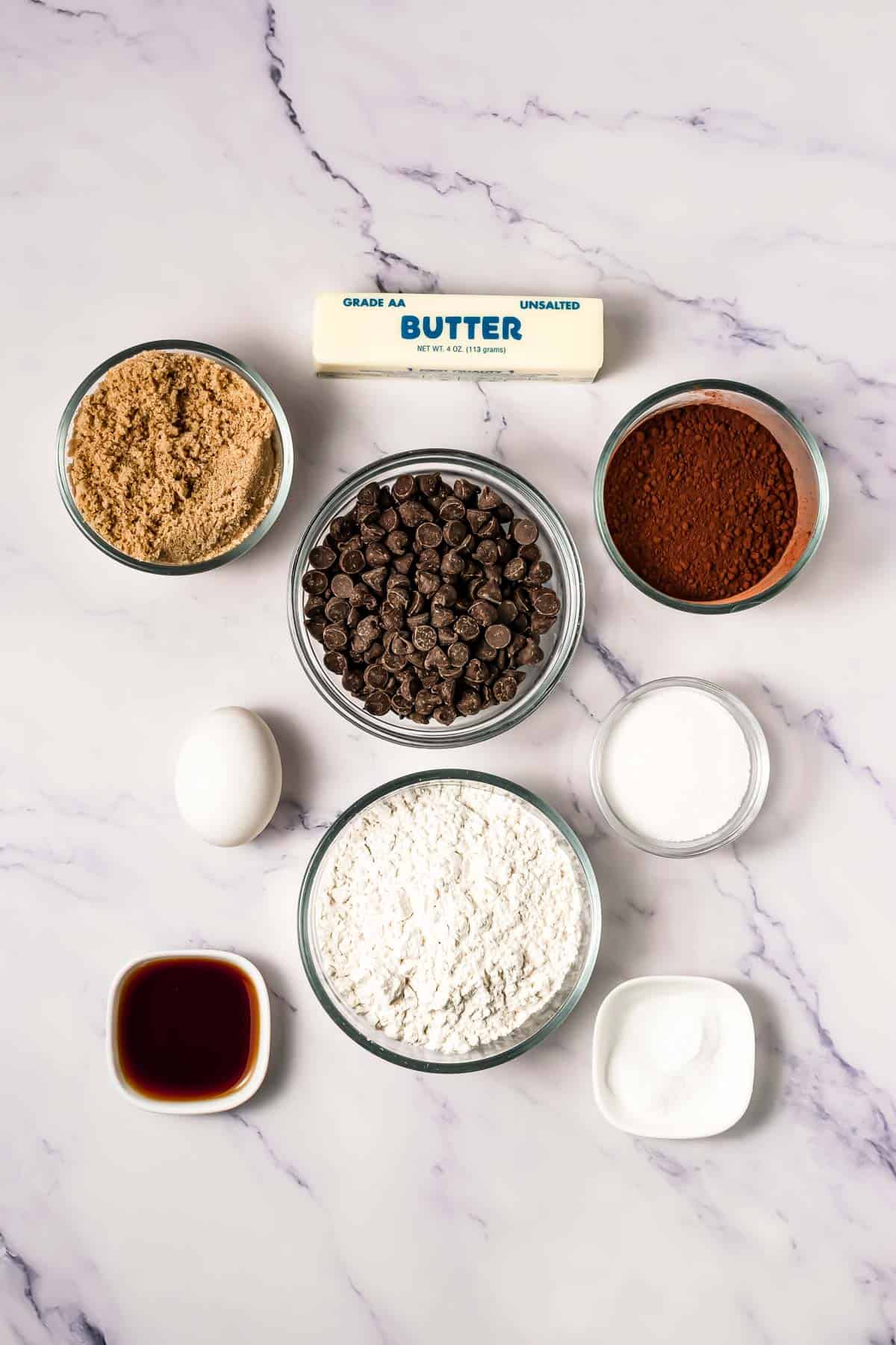 Baking ingredients on a marble surface: flour, egg, butter, cocoa, sugar, chocolate chips, vanilla, and baking soda&mdash;perfect for whipping up your own Crumbl Copycat Cookies.