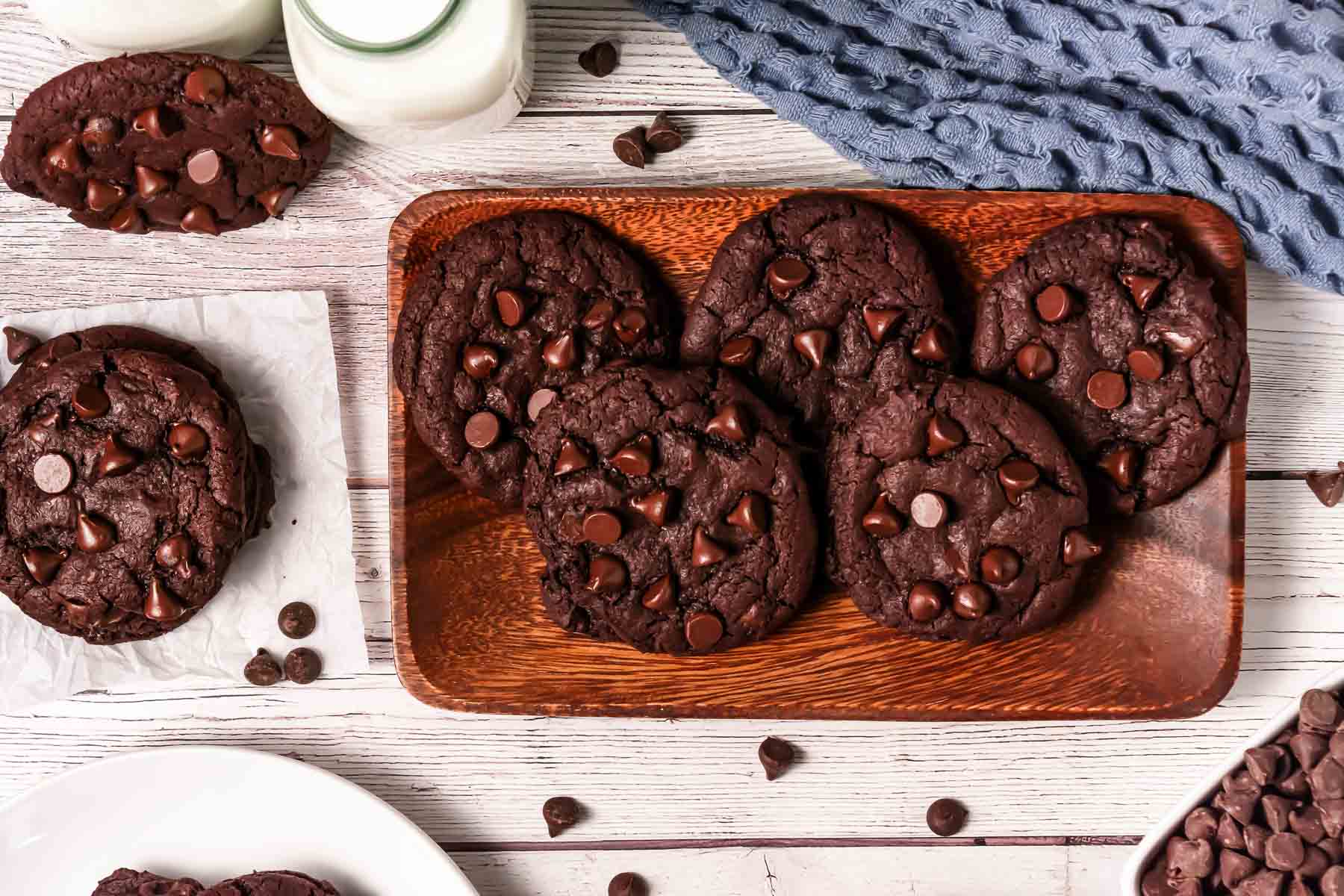 A wooden tray with six rich Dark Dream Cookies, inspired by a Crumbl Copycat recipe, surrounded by milk and extra chocolate chips.