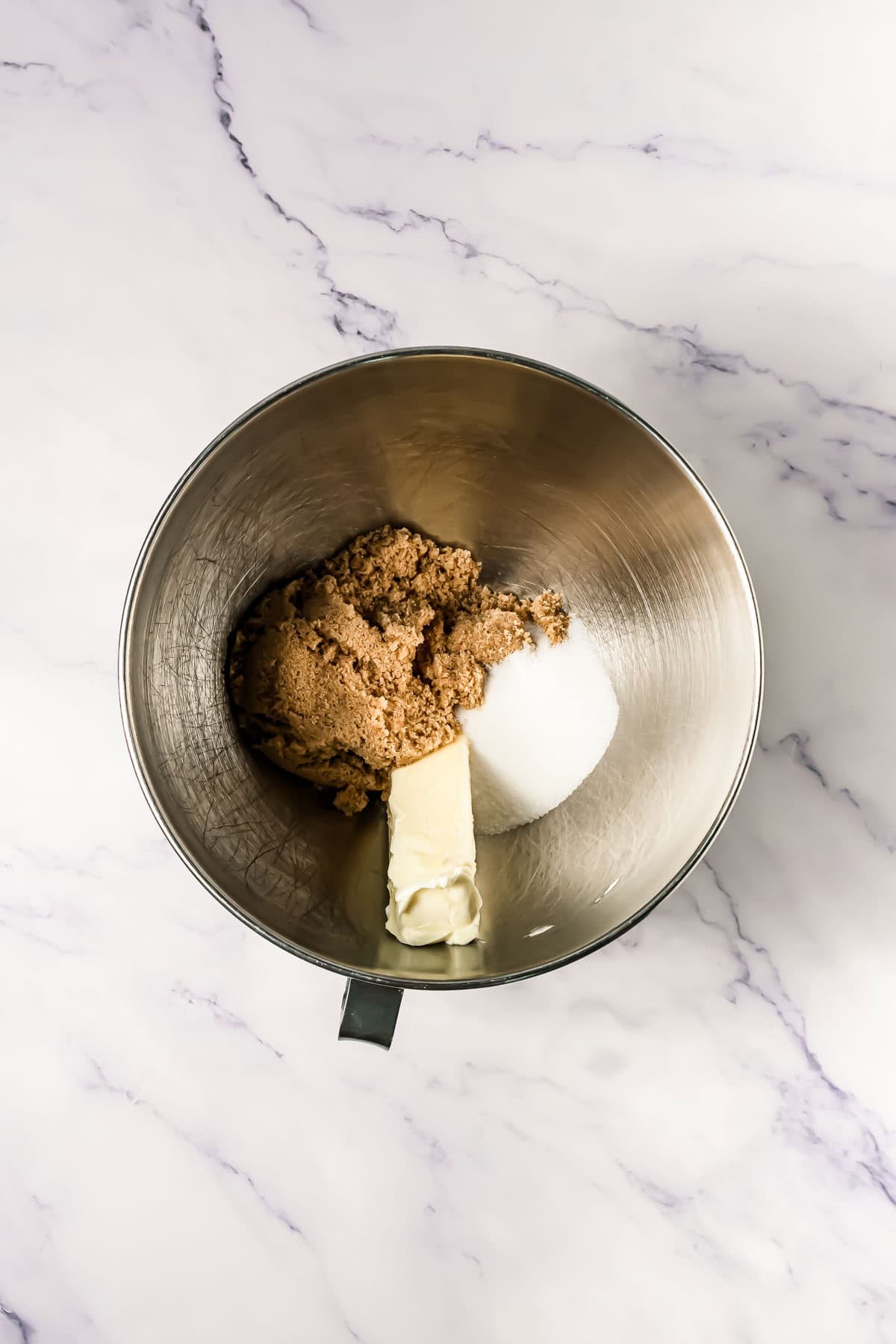 A mixing bowl with brown sugar, white sugar, and butter on a white marble surface&mdash;perfect for starting a Crumbl copycat cookies recipe.