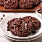 Two Copycat Cookies on a white plate, with more cookies and chocolate chips in the background—a delicious Crumbl Copycat treat.