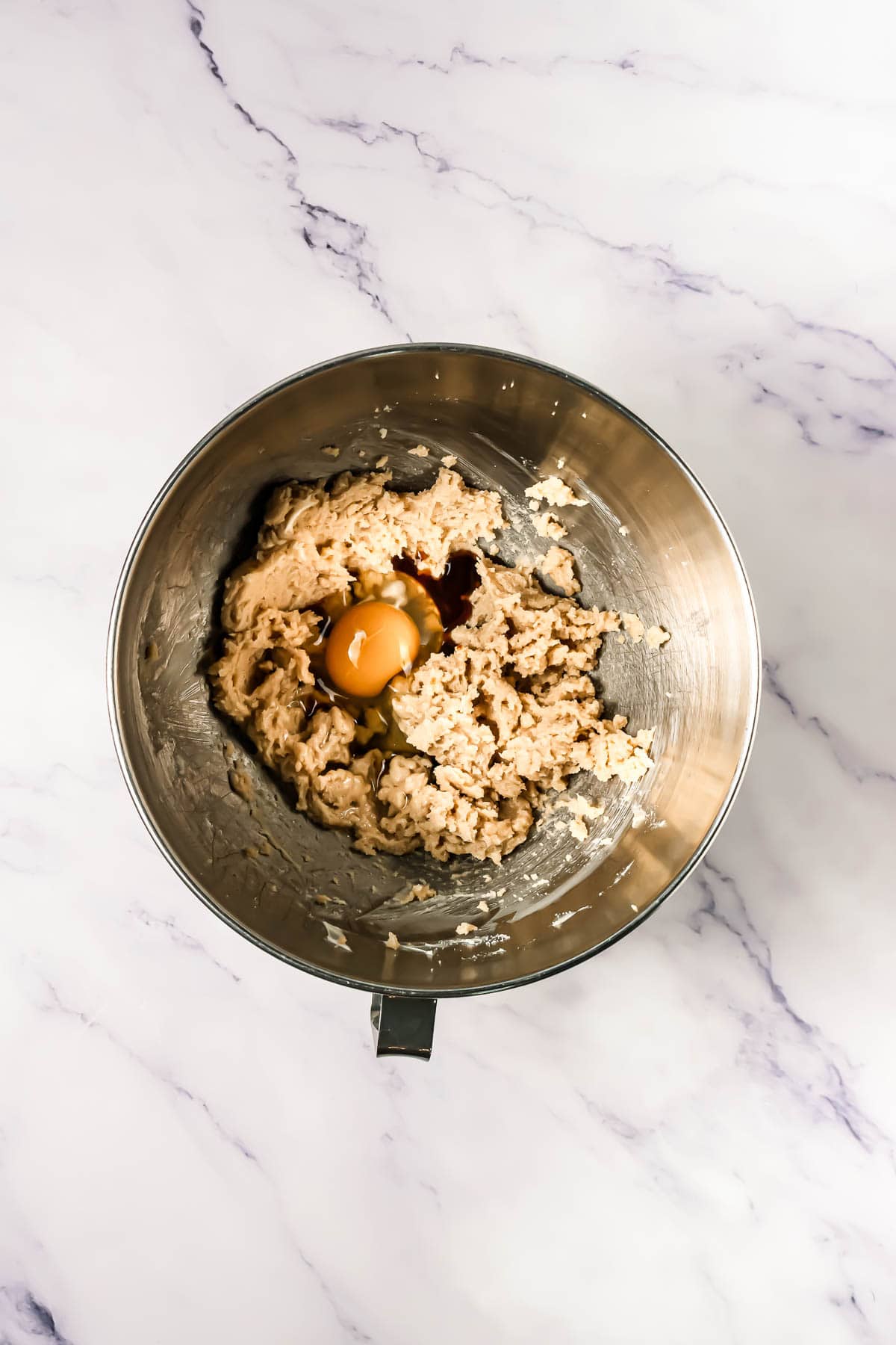 Metal mixing bowl with cookie dough, an egg, and vanilla extract on a white marble surface&mdash;perfect for baking Crumbl Copycat Dark Dream Cookies.