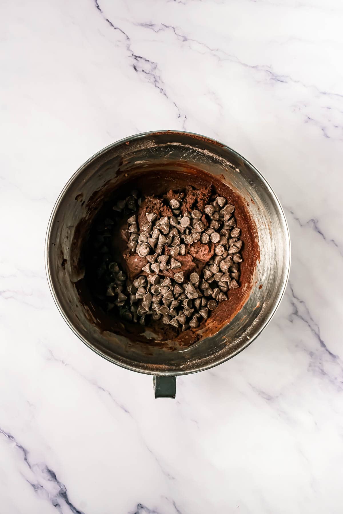 A metal mixing bowl with chocolate batter and chocolate chips on a marble countertop, perfect for making rich dark dream cookies or your favorite Crumbl copycat cookies.