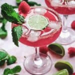 A vibrant pink Valentine's Day mocktail with ice, lime slice, mint, and raspberries in a sugar-rimmed glass.