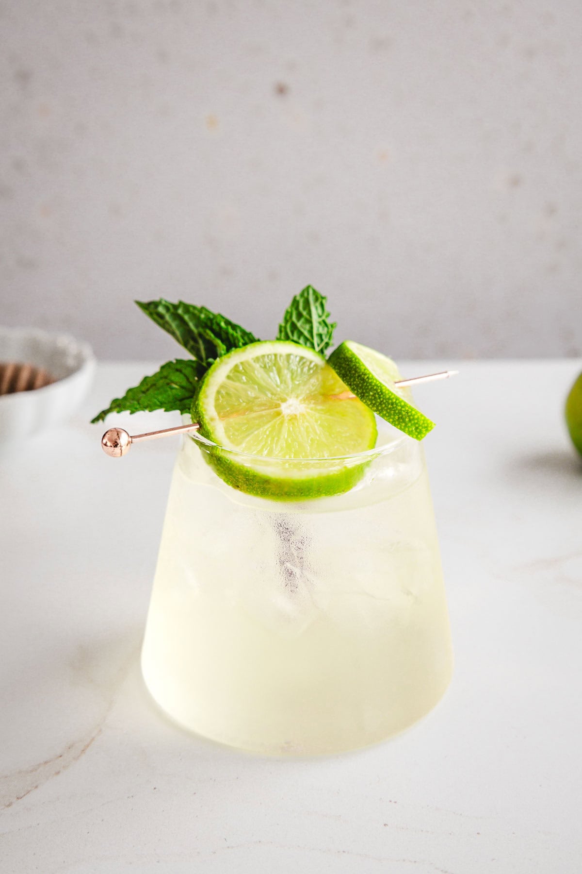 A refreshing electrolyte mocktail served in a glass with lime slices and fresh mint, set on a white surface.