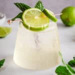 A refreshing electrolyte mocktail garnished with lime slices and mint leaves in a glass on a white surface.