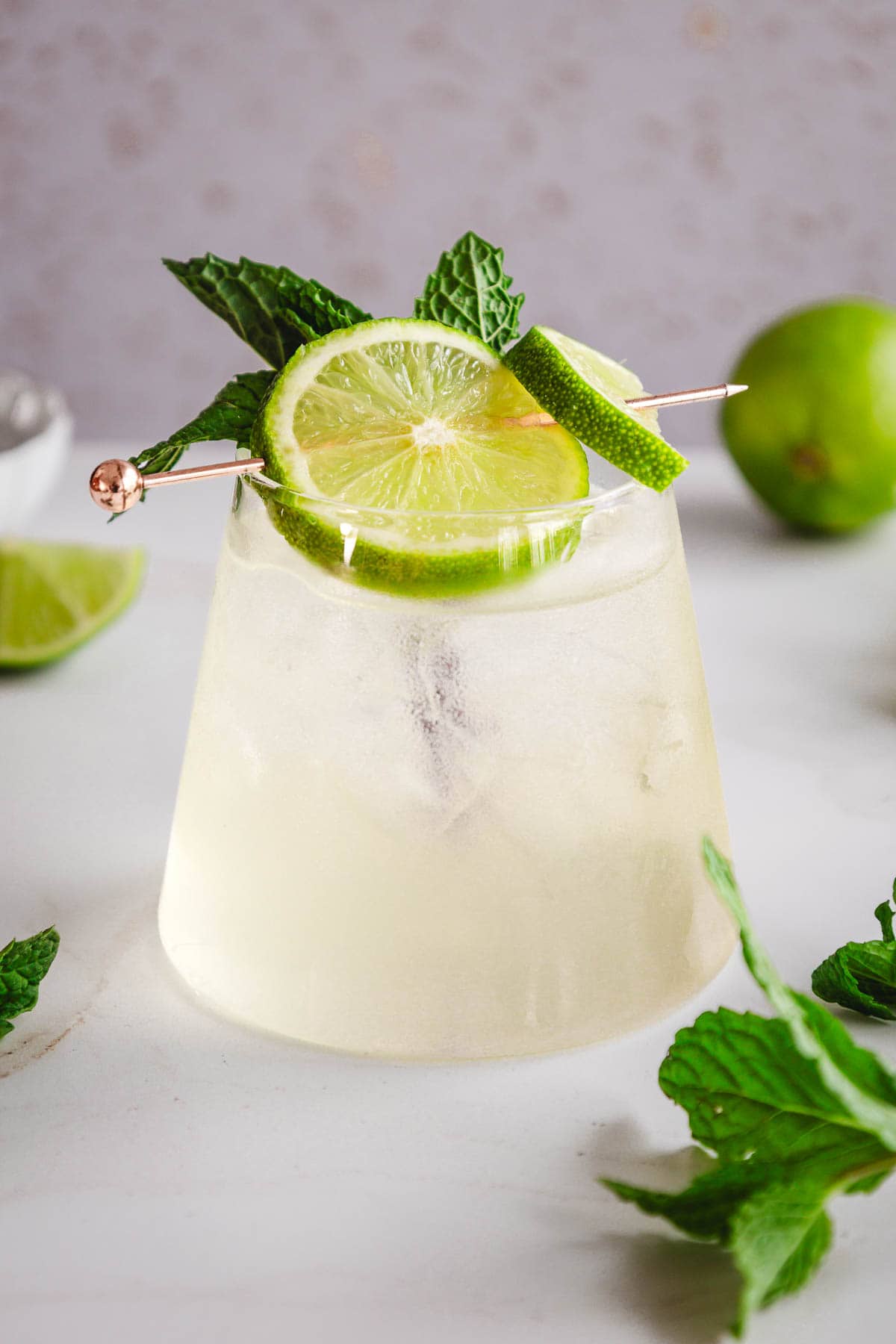 A refreshing electrolyte mocktail garnished with lime slices and mint leaves in a glass on a white surface.
