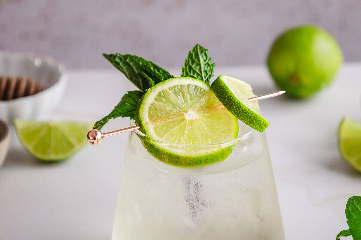 A refreshing electrolyte mocktail garnished with lime slices and mint on a cocktail pick, with limes in the background&mdash;perfect for trying a new recipe.