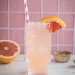 A refreshing pink grapefruit mocktail recipe served over ice in a tall glass, garnished with a grapefruit slice and striped straw—perfect for a delicious electrolyte boost.