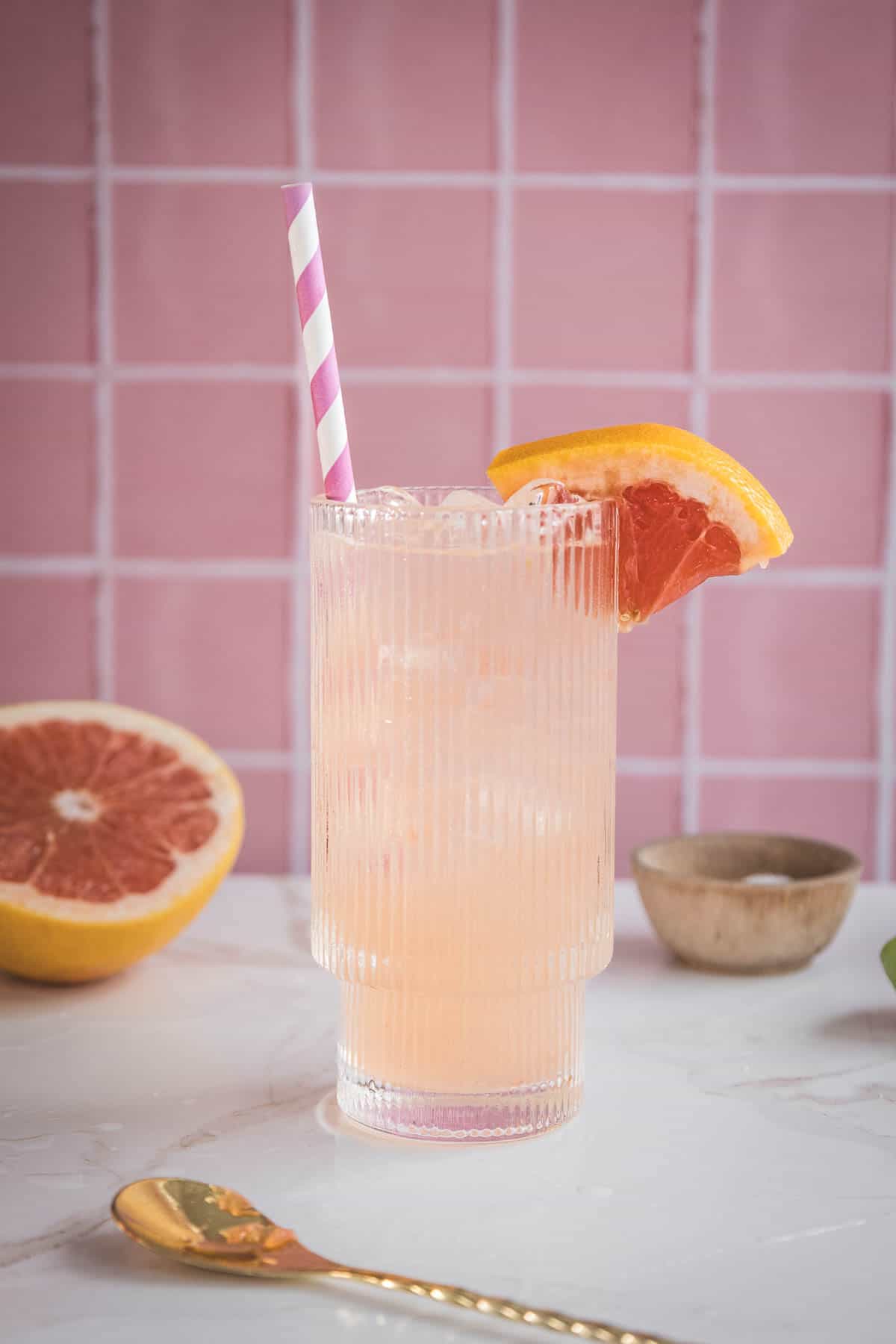 A refreshing pink grapefruit mocktail recipe served over ice in a tall glass, garnished with a grapefruit slice and striped straw&mdash;perfect for a delicious electrolyte boost.