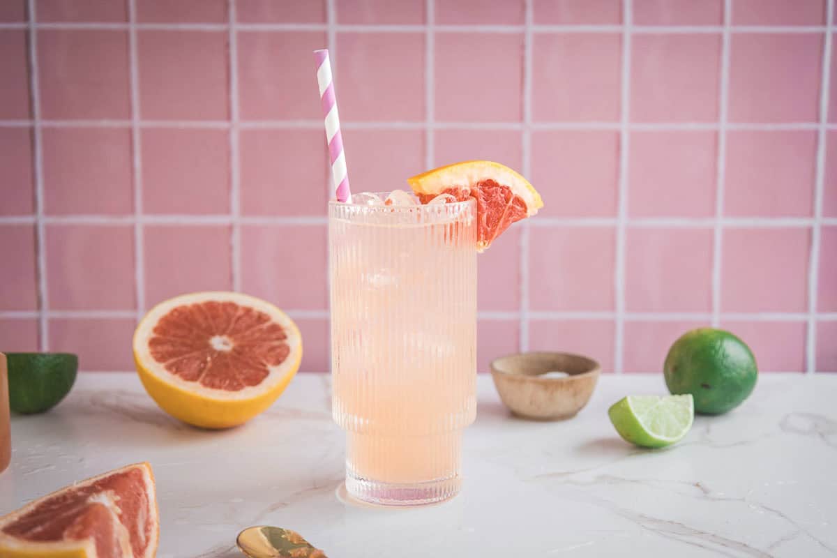 A refreshing grapefruit mocktail recipe with ice, a striped straw, and a grapefruit slice garnish, served on a marble counter&mdash;perfect for a hydrating boost of electrolytes.