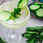 A Cucumber Margarita Mocktail garnished with cucumber slices and mint, served in a glass with a salted rim and ice.