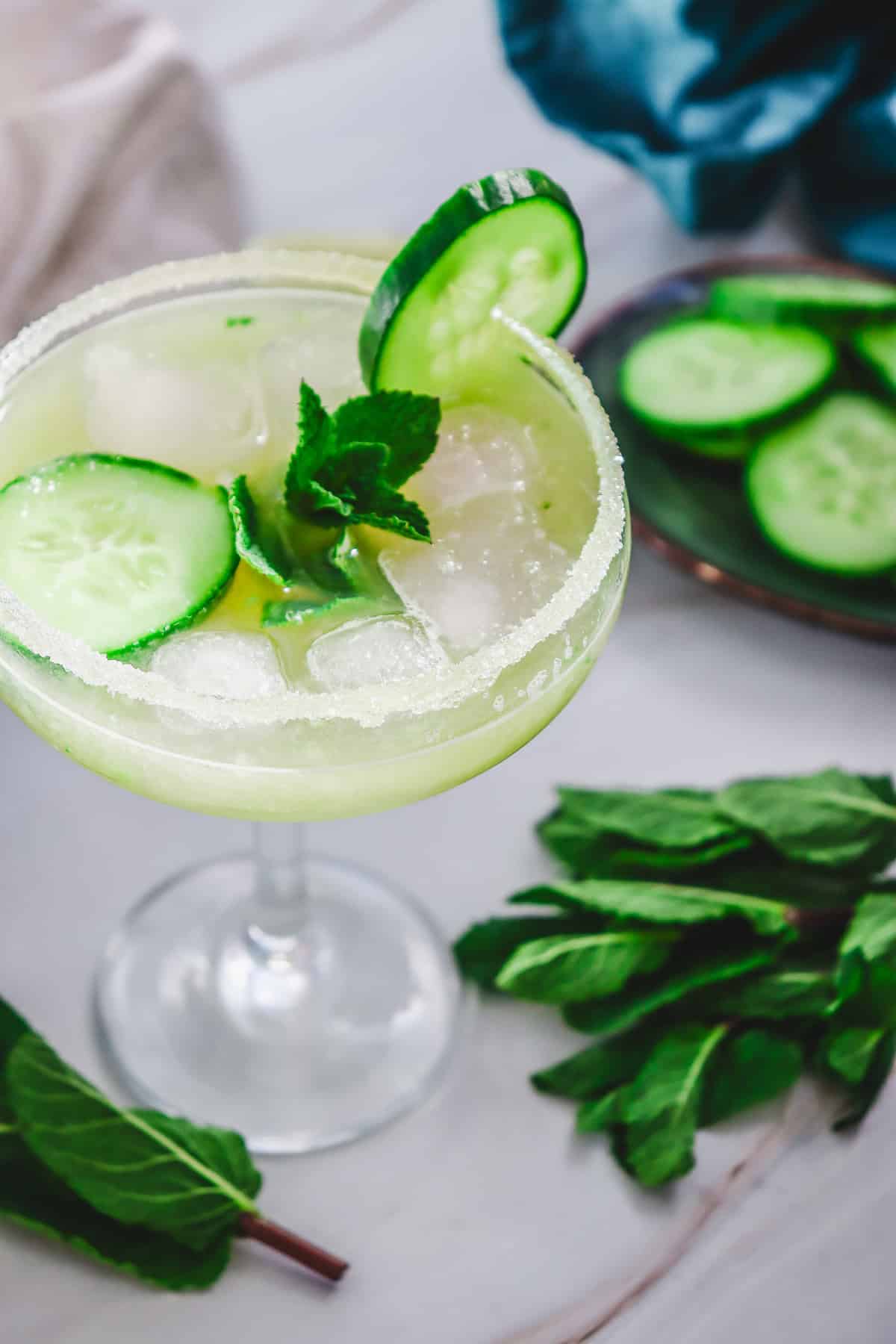 A Cucumber Margarita Mocktail garnished with cucumber slices and mint, served in a glass with a salted rim and ice.