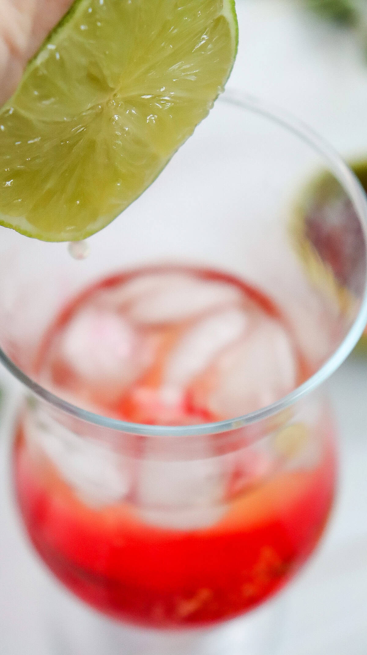A hand squeezing a lime wedge over a glass of red iced Shirley Temple Mocktail.
