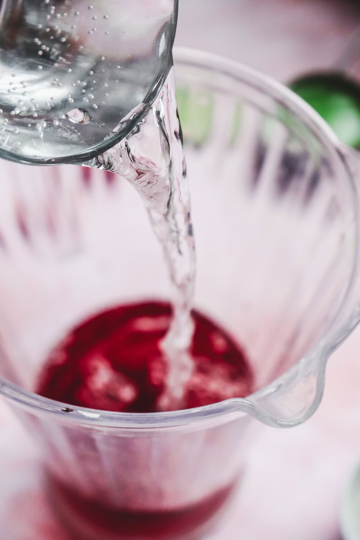 Clear liquid being poured from a glass into a blender with red ingredients inside, creating a vibrant love potion mocktail perfect for Valentine&rsquo;s Day.