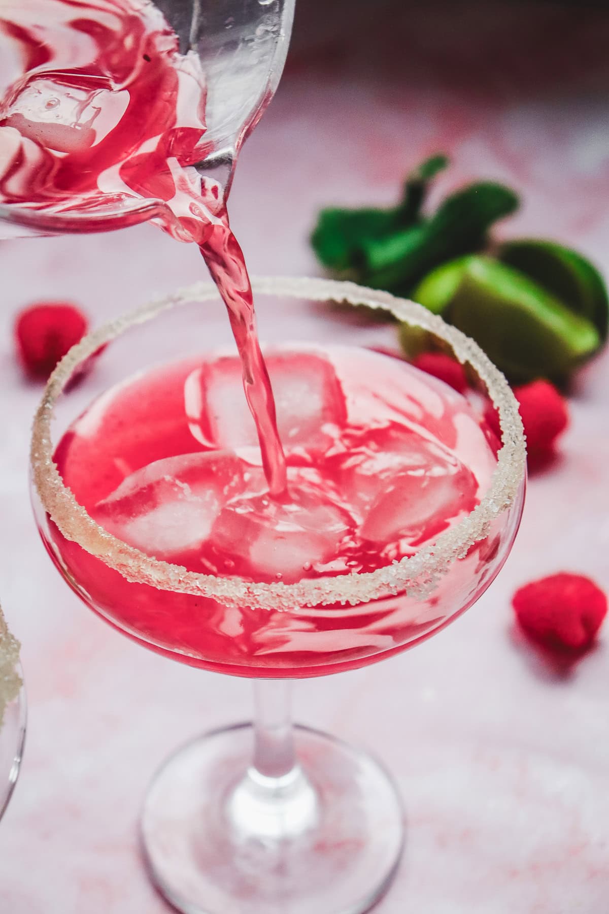 This pink Valentine's Day mocktail, served over ice in a sugar-rimmed glass, is poured to perfection with raspberries and limes in the background&mdash;like a sparkling love potion for your special celebration.