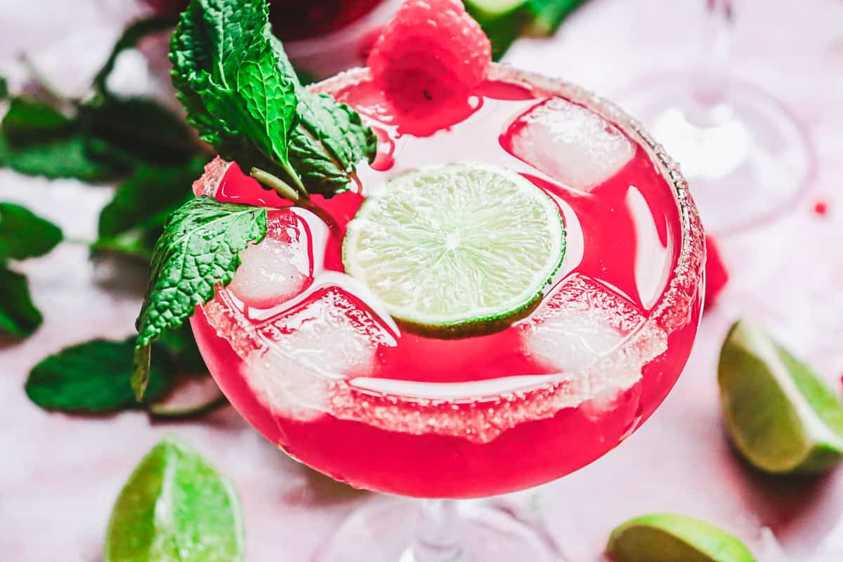 Bright pink Valentine's Day mocktail with ice, lime slice, raspberry, and mint in a sugar-rimmed glass, garnished with mint leaves&mdash;a true love potion in every sip.