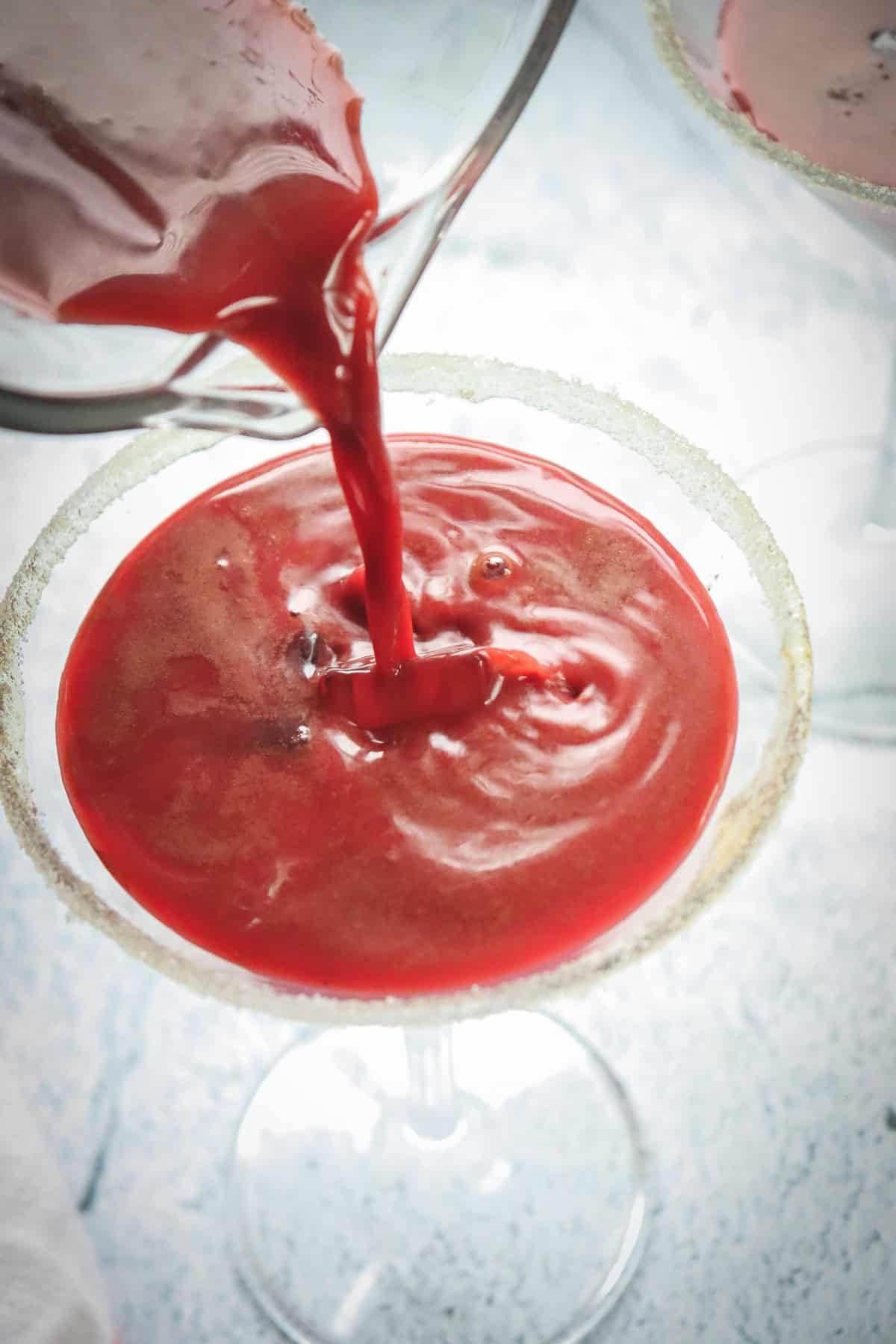Red Velvet Chocolate Martini being poured into a sugar-rimmed glass on a light surface, viewed from above&mdash;a perfect Valentine mocktail.