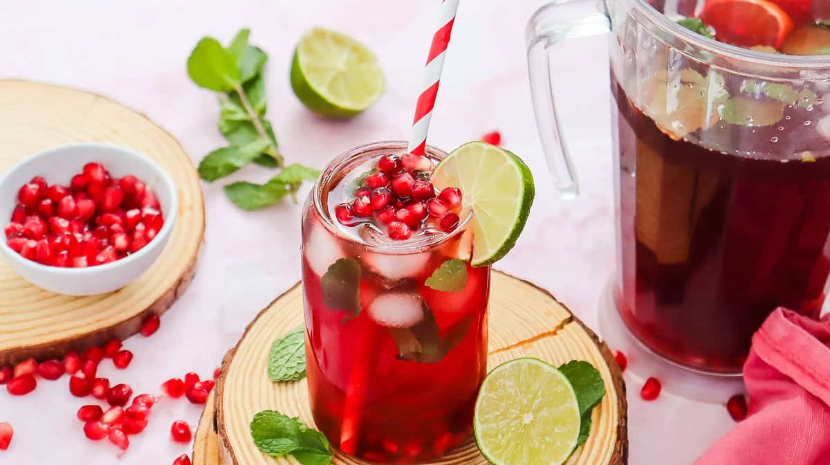 A glass of refreshing Pomegranate Fizz Mocktail with ice, lime slice, mint, and a red-striped straw, surrounded by fresh ingredients.