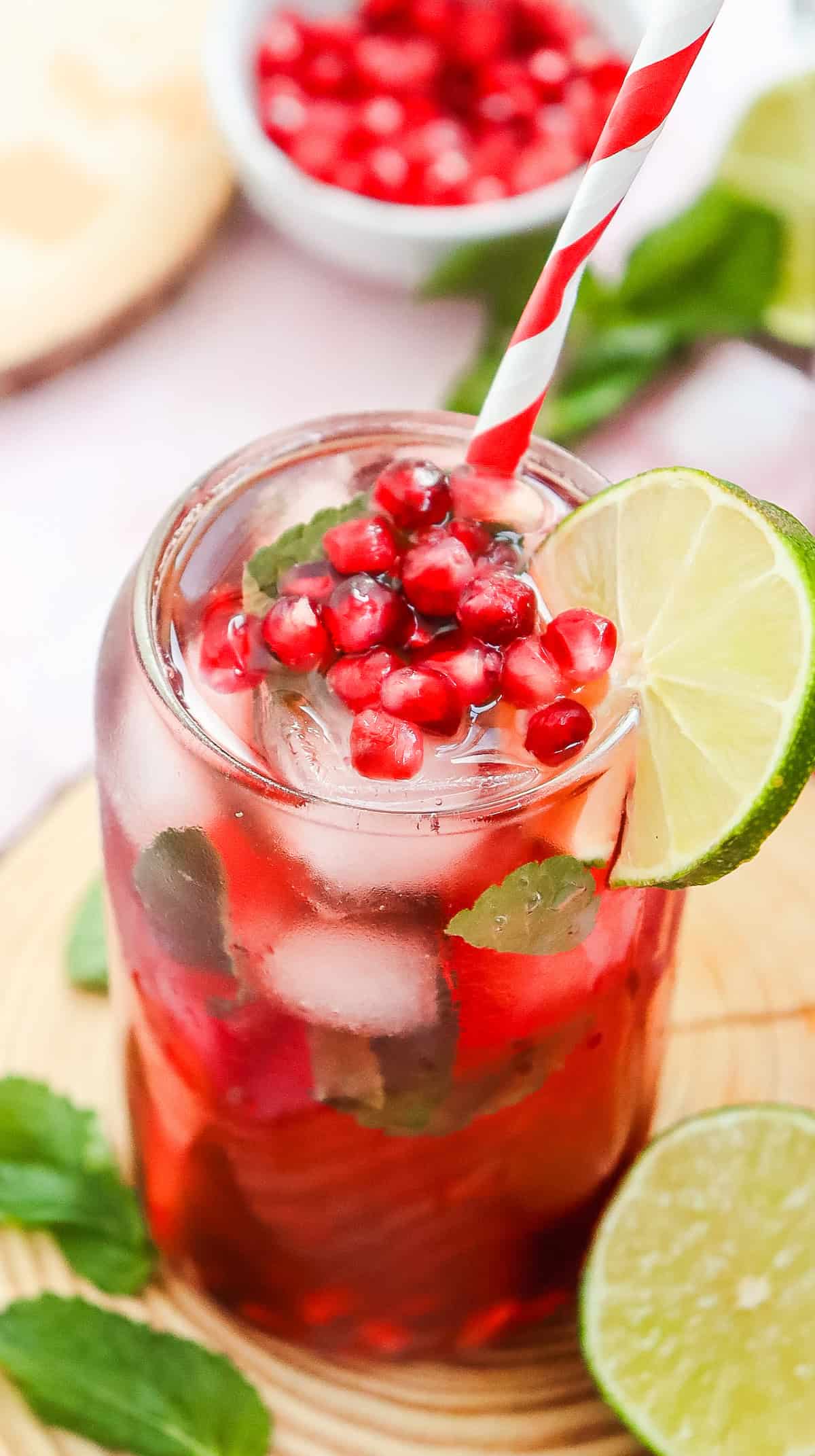 A refreshing Virgin Mocktail: a glass of iced pomegranate drink with mint, lime slice, and a red-striped straw, garnished with pomegranate seeds for a fizzy twist.