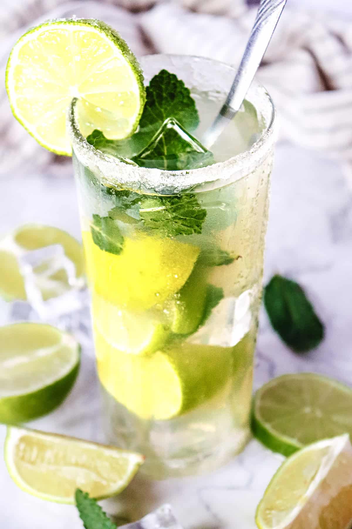 Tall glass of Classic Mojito with lime slices, mint leaves, ice cubes, and a lime wheel garnish on a light background&mdash;an inviting mocktail recipe perfect for any occasion.